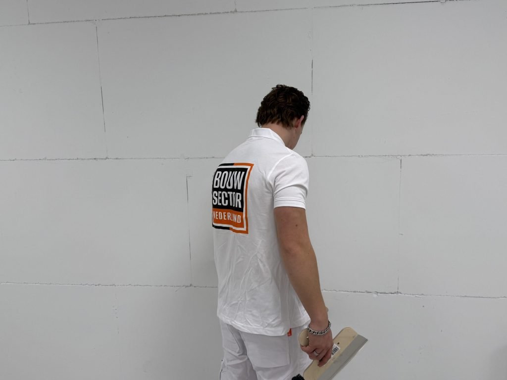 Stukadoor met een spaan in zijn hand bekijkt van dichtbij een wand van witte platen